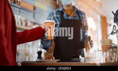 Obligatorische Gesichtsmasken und Shields in einem Coffee Shop während der Coronavirus-Pandemie. Der Kunde erhält von Barista bestellten Kaffee und Gebäck zum Mitnehmen Stockfoto