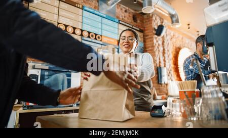 Beautiful Happy Latin Barista serviert Bestellung zu einem Food Delivery Courier Abholung Papiertüte mit Gebäck aus einem Cafe Restaurant. Delivery Guy Puts Stockfoto