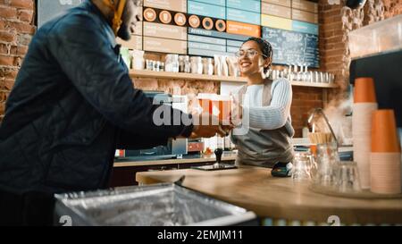 Black African American Food Delivery Courier holt zwei Kaffee und Gebäck zum Mitnehmen aus einem Cafe Restaurant. Glückliches, vielfältiges Personal gibt den Auftrag Stockfoto