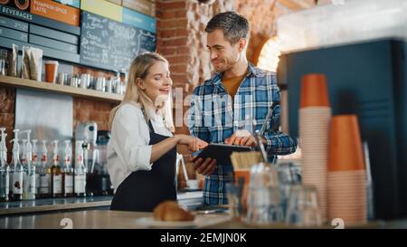 Zwei verschiedene Unternehmer haben ein Team Meeting in ihrem stilvollen Coffee Shop. Barista und Cafe-Besitzer besprechen Arbeitsplan und Menü auf dem Tablet-Computer Stockfoto