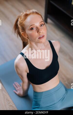 Die sportliche Rothaarige junge Frau mit Sportkleidung sitzt auf der Yogamatte im Hochwinkel. Stockfoto