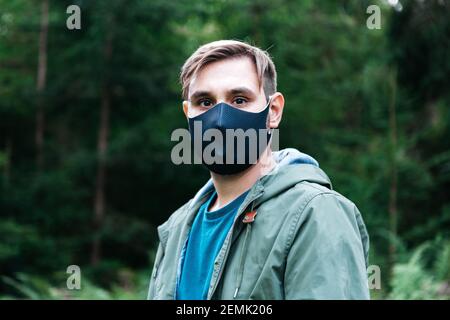 Mann in Maske reisen allein halten soziale Distanz in Bergwald durch den lokalen Tourismus. Schutz gegen Coronavirus, covid 19. Mann in Schwarz Stockfoto