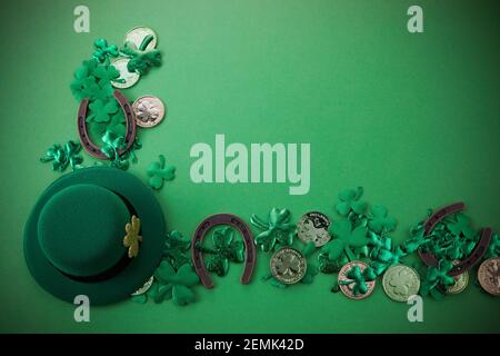 St. Patricks Day Grenze von Kleeblättern und Goldmünzen und Hufeisen über einem grünen Hintergrund. Draufsicht, flach liegend. Stockfoto