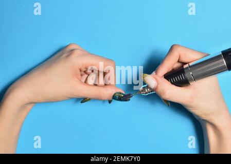 Frau grinst alte Gelnagel mit elektrischer Nagelfeile an Blauer Hintergrund Stockfoto