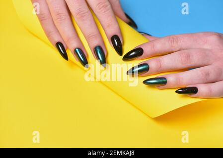 Weibliche Hände mit neuer Maniküre und dunklem Nagellack Gelber Hintergrund Stockfoto
