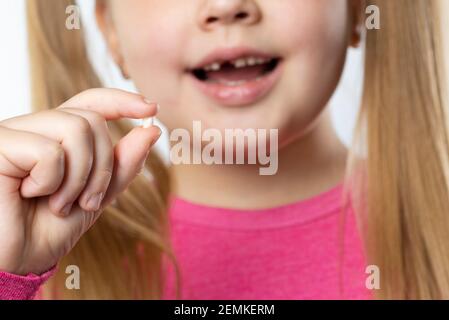 Kleine kaukasische Mädchen mit langen blonden Haaren in rosa Kleidung Hält einen herausgezogenen Milchzahn und lächelt Zahnhygiene Konzept Stockfoto