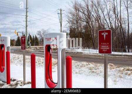 Collingwood, Ontario, Canada - 02-23-2021: Brandneue Tesla EV Elektroauto-Ladegeräte Kompressorstationen säumen den Parkplatz der Cranberry Mews Stockfoto