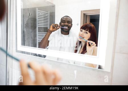 Im Badezimmer. Freudig positives multirassisches Paar, das vor dem Spiegel steht und dabei die Zähne zusammen putzt. Mundpflege und starke Zähne Co Stockfoto