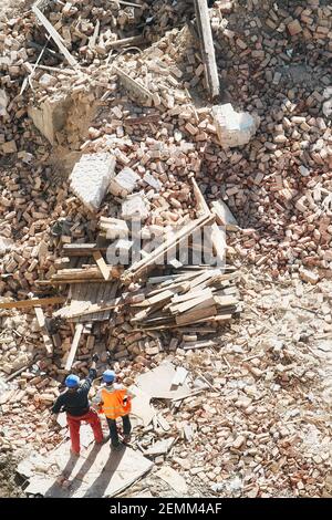 Zwei nicht identifizierte Männer inspizieren den Abriss oder die Explosionsstelle des Gebäudes, Blick von oben. Stockfoto