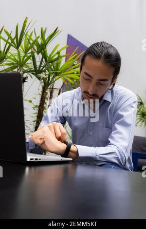 Geschäftsmann überprüft seine Smart-Uhr während der Arbeit mit seinem Computer in einer sehr entspannten Umgebung mit Pflanzen. Entspannter Geist für einen reibungslosen Arbeitsablauf Stockfoto