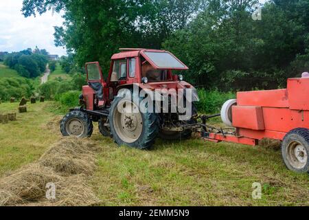 Alte rote Traktor auf dem Feld während der Heuernte Saison, Pressen Heu auf Ballen, Futter harvesting,2021 Stockfoto