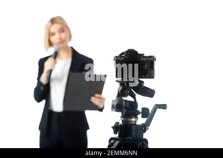 Verschwommene Anchorwoman mit Mikrofon und Klemmbrett in der Nähe von Digitalkamera isoliert Auf Weiß Stockfoto