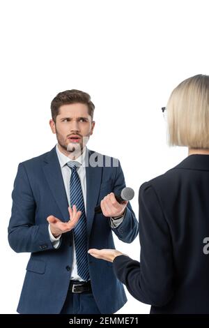 Entmutigte Journalistin mit Mikrofon gestikuliert in der Nähe blonde Geschäftsfrau während des Interviews Isoliert auf Weiß Stockfoto