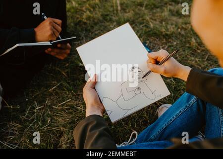 Zugeschnittenes Bild von Menschenhänden, die im Buch im Park skizzieren Stockfoto