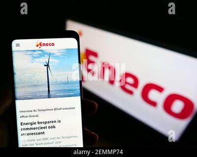 Person, die Mobiltelefon mit Logo des niederländischen Energieunternehmens Eneco Groep N.V. auf dem Bildschirm vor der Business-Webseite hält. Fokus auf der Mitte des Telefondisplays. Stockfoto