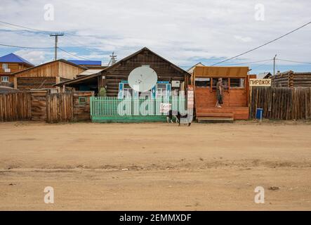 Holzhaus mit Satellitenschüssel. In der Nähe gibt es einen Lebensmittelkiosk mit kleinen Schilder-Ankündigungen in Russisch "WIR VERMIETEN ZIMMER", "FISCH, TEE, KAFFEE, BÄCKEREI T Stockfoto