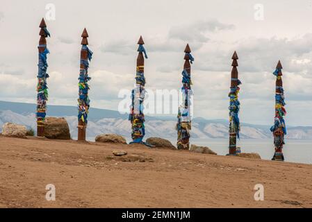 Eine Reihe von Sergen in Shamanka auf Olchon Island. Reihe von 6 hohen Ritual Buryat religiösen Säulen mit farbigen Bändern gebunden, vor dem Hintergrund blau Stockfoto