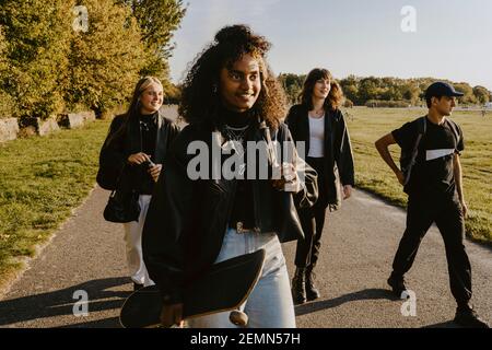 Junge Frau hält Skateboard, während Sie mit Freunden im Park spazieren Stockfoto