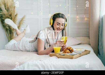 Attraktive kaukasische Frau auf dem Bett im Schlafzimmer liegt hat Video-Chat im Telefon, kommuniziert und lacht. Stockfoto