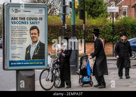 London, Großbritannien. Februar 2021, 25th. Die Menschen passieren staatliche Hinweisschilder (sind die Impfstoffe sicher?) Während sie sich auf Purim in Stamford Hill vorbereiten, einem der Gebiete mit der höchsten Inzidenz von Covid 19 Infektionen in London. Purim ist ein jüdisches 24-Stunden-Festival, das das Überleben der vom Aussterben bedrohten Juden in Persien feiert. Sie kaufen Mishloach Manos Geschenke von Lebensmitteln an Familie und Freunde. National Lockdown 3 mit der Anweisung der Regierung, dass alle zu Hause bleiben, um den Druck auf den NHS zu retten. Kredit: Guy Bell/Alamy Live Nachrichten Stockfoto