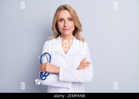 Foto von reifen seriösen professionellen Frau Arzt mit gekreuzten Händen Stethoskop auf grauem Hintergrund isoliert halten Stockfoto