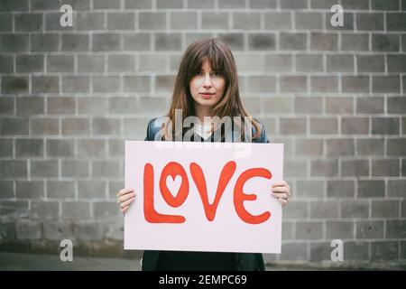 Portrait einer Aktivistin mit Liebesposter gegen die Wand Stockfoto