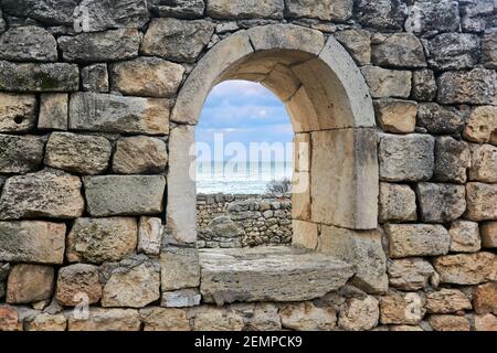 Halbrunde Fenster öffnet sich in den Ruinen einer antiken Wand, hinter dem Sie das Meer sehen können Stockfoto