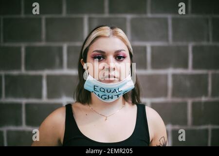 Junge Frau trägt Schutzmaske mit gleichen Rechten Text An der Wand Stockfoto