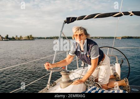 Ältere Frau, die den Griff dreht, während sie im Boot auf See segelt Sonniger Tag Stockfoto