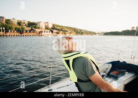 Älterer Mann, der am sonnigen Tag im Boot gegen den Himmel lachend ist Stockfoto