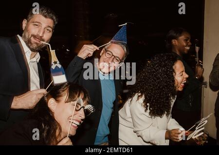 Fröhliche Geschäftsleute mit Requisiten genießen die Party in der Gesellschaft am Abend Stockfoto