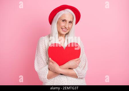 Porträt von attraktiven zarten fröhlich grauhaarigen älteren Frau Rentner umarmt Herz Zeichen Zuneigung amour isoliert über rosa Pastellfarben Hintergrund Stockfoto