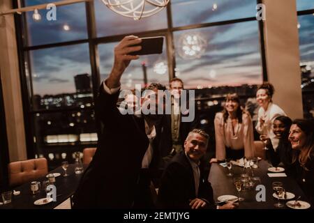 Lächelnde Geschäftsleute, die im Büro Selfie auf dem Mobiltelefon machen Während der Party Stockfoto