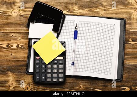 Office-Tools im Vintage-Hintergrund, Draufsicht. Organizer, Rechner, Locher, Notizpapier, Stift. Geschäfts- und Arbeitskonzept. Schreibwaren und lederbezogene Notizbücher, offen mit leeren Seiten. Stockfoto
