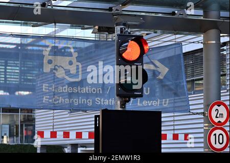 München, Deutschland. Februar 2021, 25th. E-Ladestation Informationsbanner auf einem Parkhaus der Messe in München Riem hinter einer roten Ampel. Quelle: dpa/Alamy Live News Stockfoto