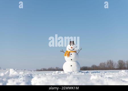 Lustige Schneemann in stilvollen braunen Hut und gelben Skalf auf schneebedeckten Feld. Blauer Himmel auf dem Hintergrund Stockfoto