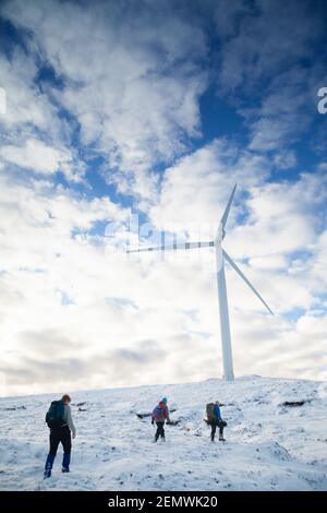 Drei Bergwanderer, die im Millennium an einer Turbine vorbeilaufen Windfarm auf Meall Dubh in den schottischen Highlands Stockfoto