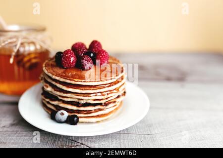 Saftige Pfannkuchen mit Beeren und Honig auf einem weißen Teller, Löffel, Glas, Holztisch. Hochwertige Fotos Stockfoto
