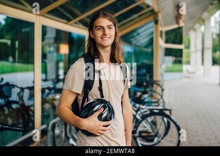 Porträt eines lächelnden männlichen Studenten mit Fahrradhelm am Fahrrad Parkstation auf dem Campus Stockfoto