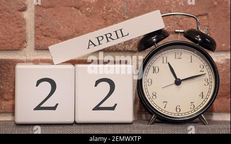 Wichtiger Termin, 22. April, Frühjahrssaison. Kalender aus Holz auf dem Hintergrund einer Ziegelwand. Retro-Wecker als Zeitmanagement-Konzept. Stockfoto