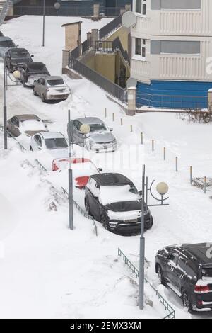 Moskau / Russland - Februar 13 2021: Autos auf der Straße Parkplatz in der Nähe von Wohngebäude unter dicken Schicht von Schnee, ein Auto wurde rechts auf der Straße stecken, nach n Stockfoto