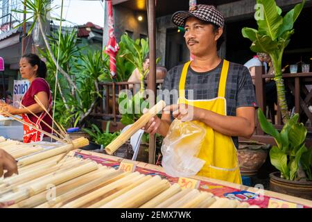 Street Food Markt in Asien. Ein Mann verkauft Reis in Bambusstielen. Stockfoto