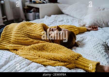 Frau mit erhobener Hand, die zu Hause auf dem Bett liegt Stockfoto