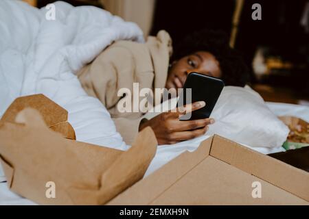 Junge Frau mit Mobiltelefon von Bett zu Hause liegen Stockfoto