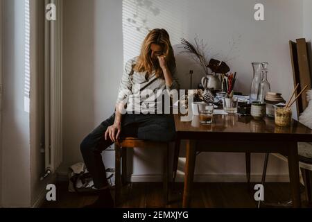 Deprimierte Frau sitzt auf einem Stuhl im Wohnzimmer Stockfoto