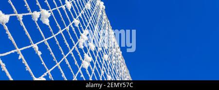 Volleyballnetz mit Schnee bedeckt gegen blauen Himmel an klaren Wintertag. Minimalismus der Natur. Bannerformat. Stockfoto