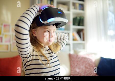 Ziemlich junges Mädchen trägt Virtual Reality-Headset zu Hause. Nettes Kind mit VR-Brille ein Spiel zu spielen. Kind im virtuellen Augmented Reality Helm. Zukunft Stockfoto