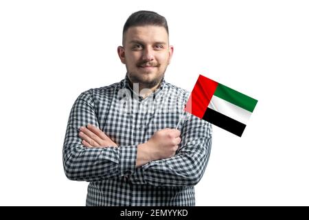 Weißer Kerl hält eine Flagge der Vereinigten Arabischen Emirate lächelnd zuversichtlich mit gekreuzten Armen isoliert auf einem weißen Hintergrund. Stockfoto