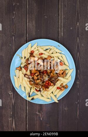 Gesunde nahrhafte Mahlzeit mit Waldpilzen. Pasta Penne mit goldenen Pfifferlingen und Chilischoten in blauer Platte auf dunklem Holzhintergrund Stockfoto