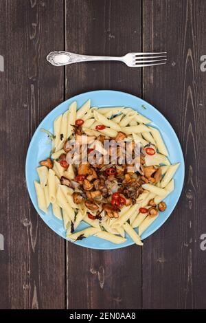 Vegetarische Mahlzeit mit Waldpilzen. Pasta Penne mit goldenen Pfifferlingen in blauer Platte auf dunklem Holzhintergrund Copyspace Overhead-Ansicht Stockfoto